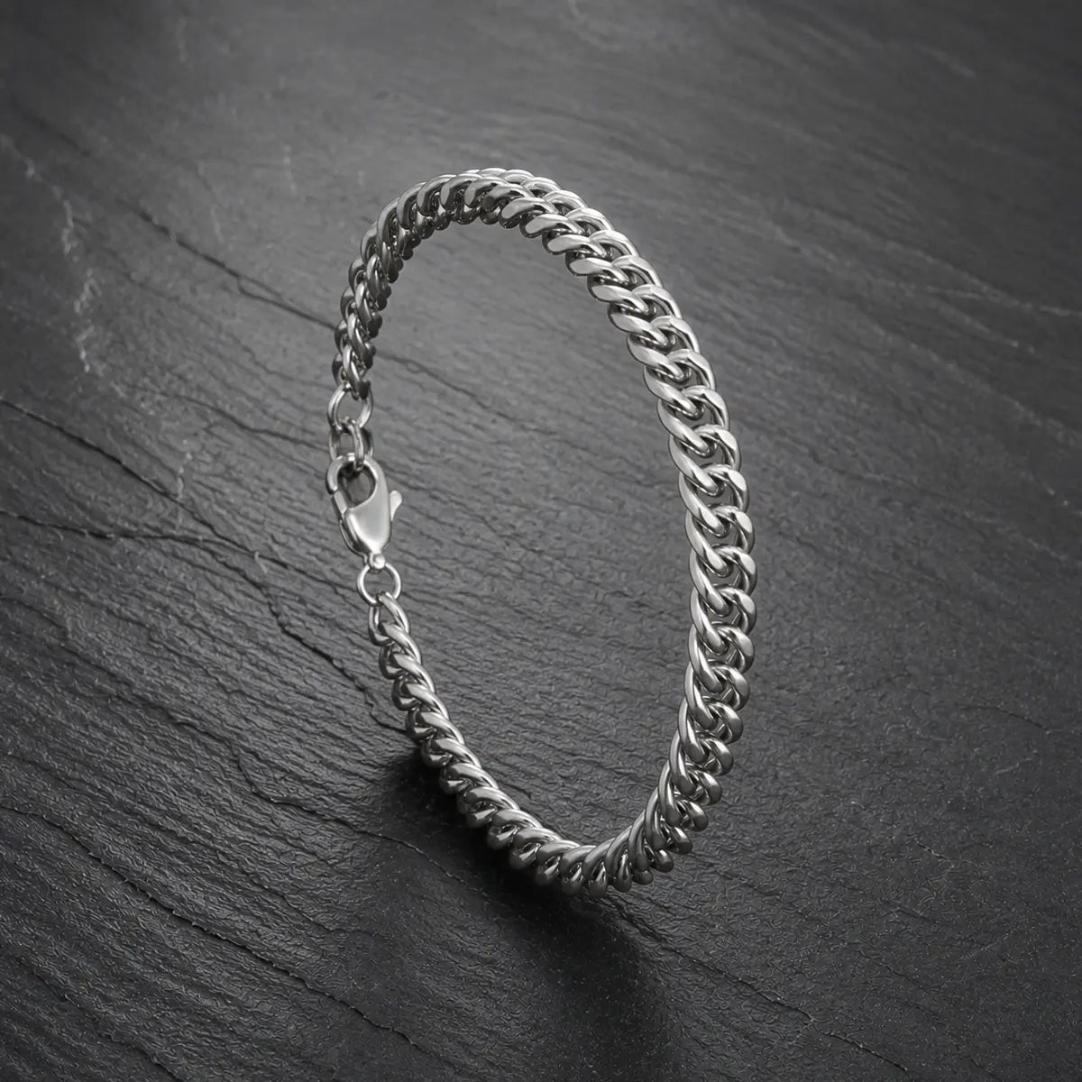 Silberfarbenes Herren Armband aus Edelstahl mit Karabinerverschluss auf dunkler Steinoberfläche.