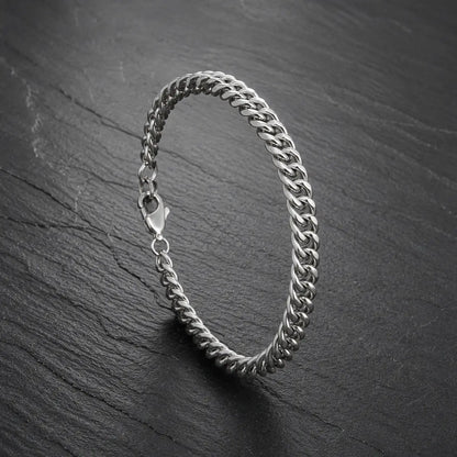 Silberfarbenes Herren Armband aus Edelstahl mit Karabinerverschluss auf dunkler Steinoberfläche.