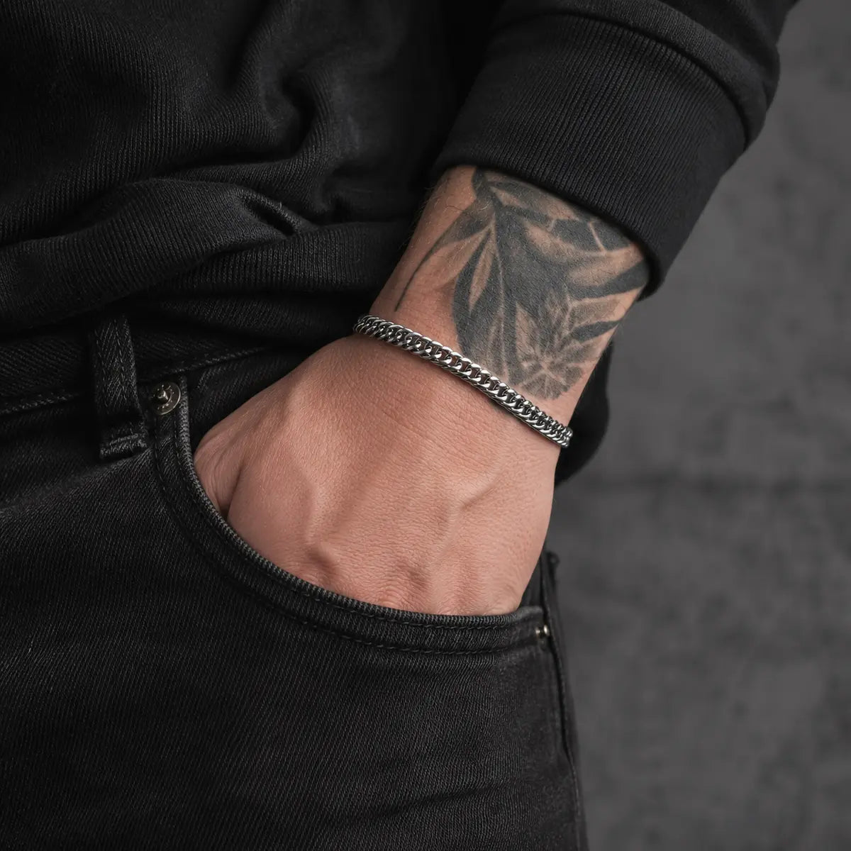 Silberfarbenes Herren Armband aus Edelstahl am tätowierten Handgelenk getragen.