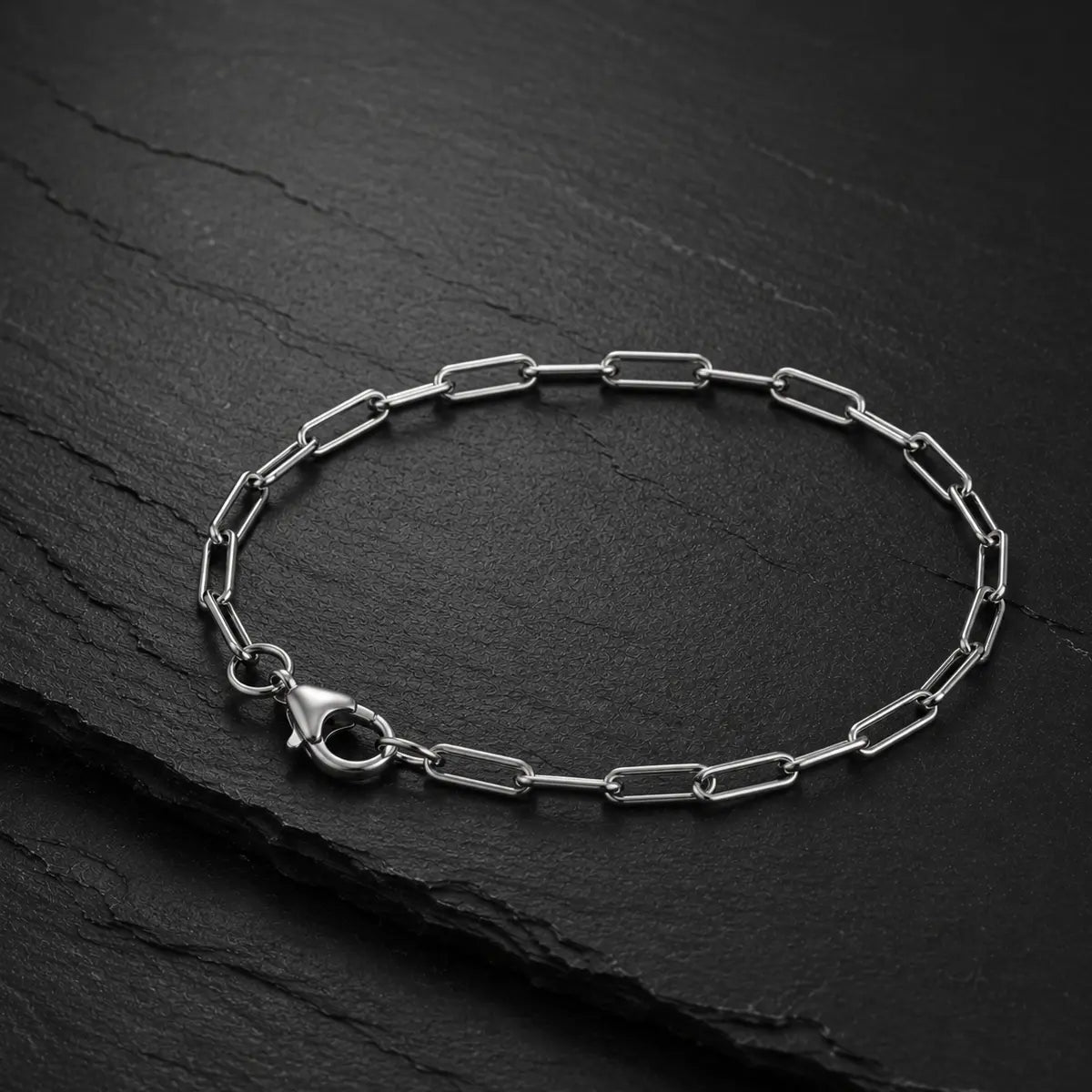 Feines Paperclip Herren Armband mit Karabinerverschluss aus silberfarbenem Edelstahl auf dunkler Schieferplatte.