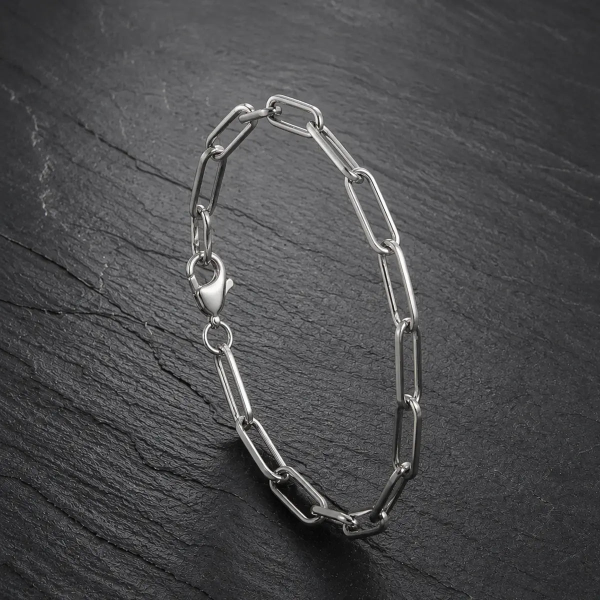 Silberfarbenes Paperclip Herren Armband aus Edelstahl auf dunkler Schieferplatte.