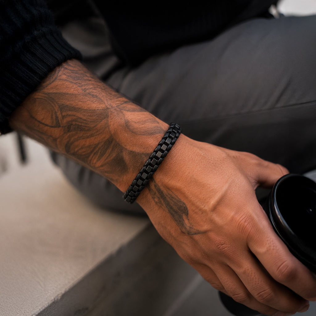 Schwarzes Herren Lederarmband mit Edelstahlelementen am tätowierten Handgelenk getragen.