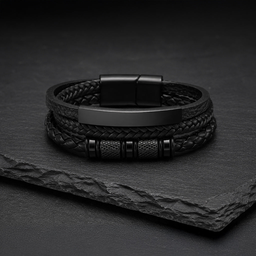 Mehrsträngiges schwarzes Herren Lederarmband mit Gravurplatte auf dunkler Schieferplatte.