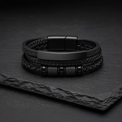 Mehrsträngiges schwarzes Herren Lederarmband mit Gravurplatte auf dunkler Schieferplatte.